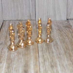 May include: Six gold-coloured chess pieces, including a king, queen, and rook, are arranged in a row on a wooden surface.