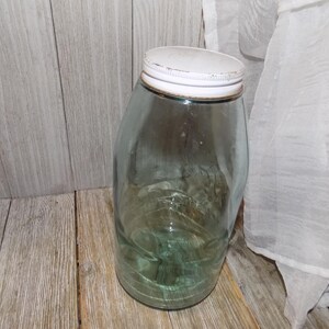 May include: A large, clear glass jar with a white lid. The jar has a textured surface and is slightly tinted green.