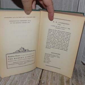 May include: A vintage book with a green cover titled "The Enormous Room" by E.E. Cummings. The book is open to a page with a note on the author and a bibliography of their works.