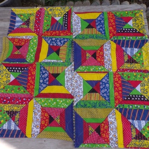 May include: A colorful patchwork quilt with a geometric pattern of squares and triangles. The quilt is made of various fabrics in shades of red, green, blue, yellow, and white.