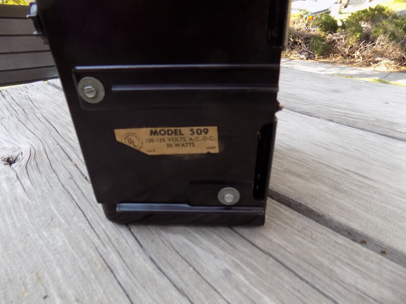 Puede incluir: Un dispositivo electr&oacute;nico vintage de color marr&oacute;n oscuro con forma rectangular. Una etiqueta en el lateral dice "MODELO 509" e incluye especificaciones el&eacute;ctricas. El dispositivo est&aacute; asegurado con sujetadores met&aacute;licos.