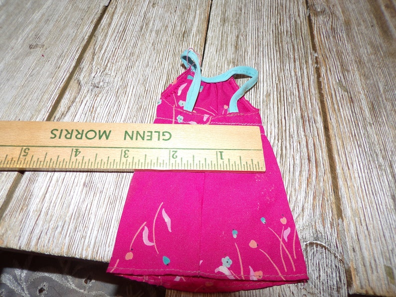 May include: A pink sleeveless dress with a floral print and a light blue ribbon tie at the top. The dress is approximately 6 inches long.