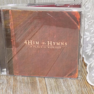 May include: A CD case featuring the album "4Him Hymns: A Place of Worship." The album cover has a brown, textured design with the album title and text in a light brown font. The CD case is clear.