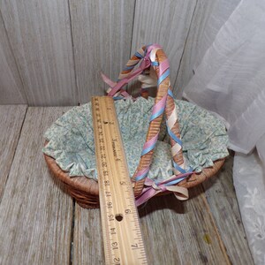 Peut inclure: Un petit panier en osier avec une doublure florale bleu et blanc et des anses en ruban rose et bleu.