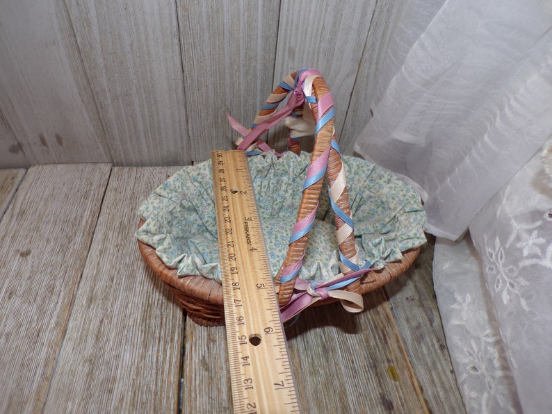 Peut inclure: Un petit panier en osier avec une doublure florale bleu et blanc et des anses en ruban rose et bleu.