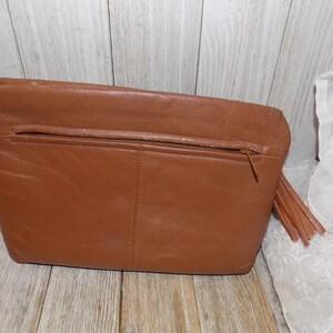 May include: A brown leather clutch purse with a zipper closure and a tassel. The purse has a simple design and is made of high-quality leather.