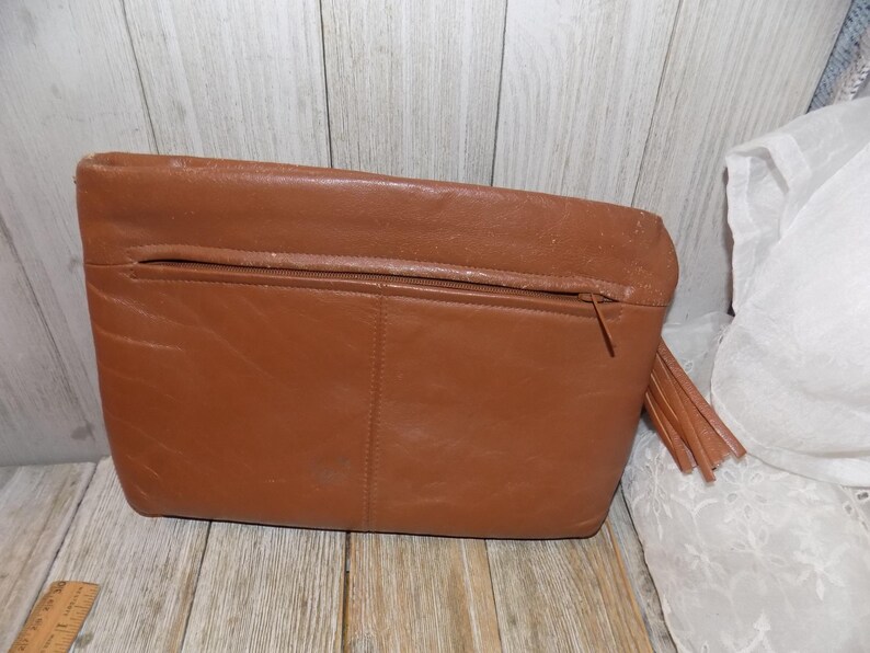 May include: A brown leather clutch purse with a zipper closure and a tassel. The purse has a simple design and is made of high-quality leather.