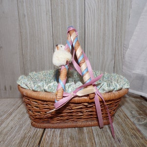 Peut inclure: Un petit panier en osier avec une doublure florale et des anses en ruban rose et bleu. Le panier est vide et pr&ecirc;t pour les &oelig;ufs de P&acirc;ques.