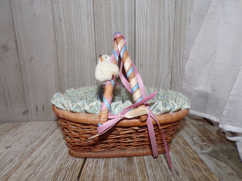 Peut inclure: Un petit panier en osier avec une doublure florale et des anses en ruban rose et bleu. Le panier est vide et pr&ecirc;t pour les &oelig;ufs de P&acirc;ques.