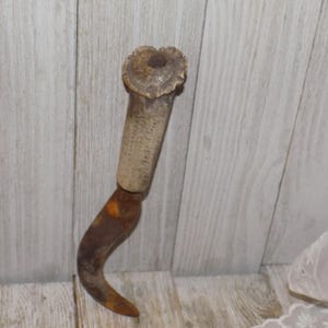 May include: A rusty, curved metal hook with a wooden handle. The handle is made of antler and has a carved design.