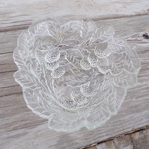 May include: A clear glass bowl with a leaf and berry design. The bowl is perfect for serving snacks or fruit.