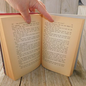 May include: Open book with a cream-colored cover and black text. The text on the left page reads "The Shadow of the Boint" and the text on the right page reads "Drop the Gun!"