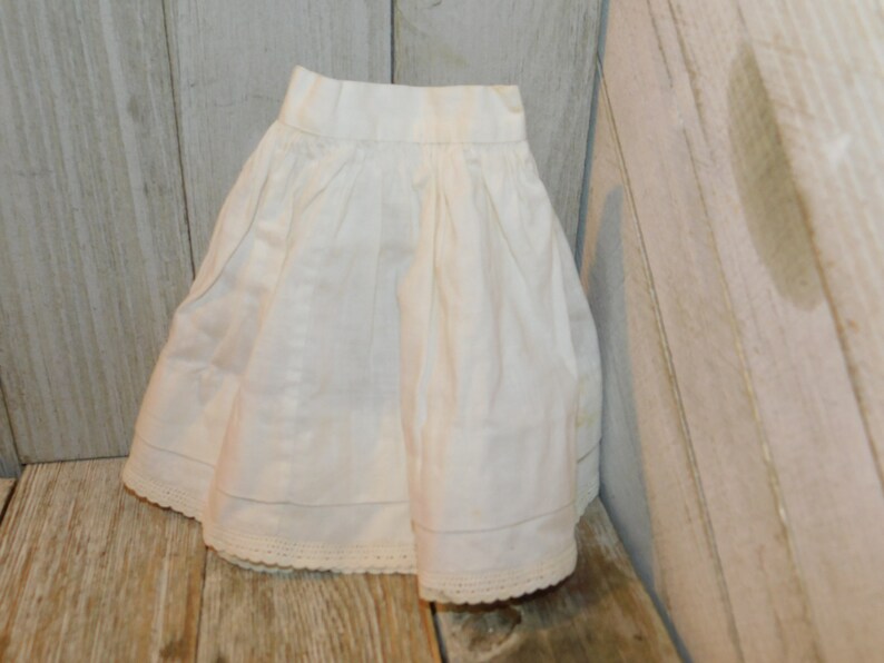 May include: A white cotton skirt with a lace trim. The skirt is gathered at the waist and has a simple, classic design.