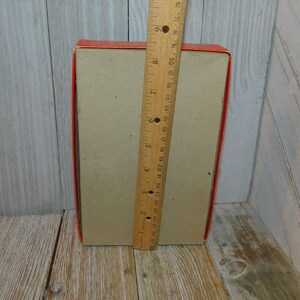 May include: A red and brown cardboard box with a ruler next to it. The box is approximately 7 inches tall.