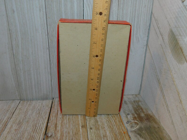 May include: A red and brown cardboard box with a ruler next to it. The box is approximately 7 inches tall.