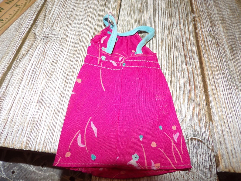 May include: A pink sleeveless dress with a floral print and blue straps. The dress is made of a soft, lightweight fabric.