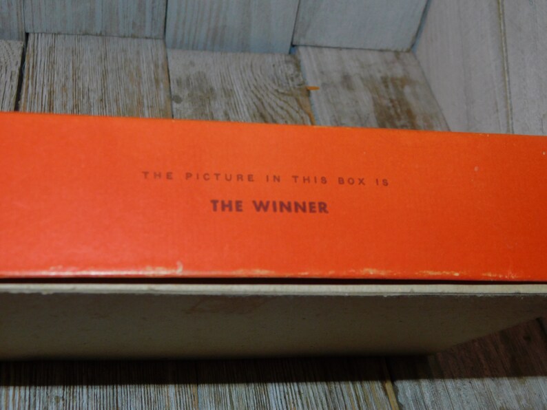 May include: Close-up of an orange box with the text "THE PICTURE IN THIS BOX IS THE WINNER" printed on it.