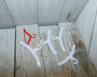 May include: Five white plastic hangers with a single red plastic hanger. The hangers have a hook on one end and a curved shape on the other end.