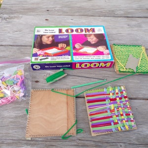 May include: A vintage De Luxe two-sided loom kit for weaving. The kit includes a loom, yarn, a hook, and a bag of colorful plastic loops. The box features a photo of two children using the loom.