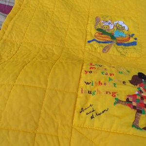 May include: Bright yellow quilt with embroidered images and text. One image depicts two figures in a boat, the other shows two figures embracing. Text includes "Love me...without laughing."