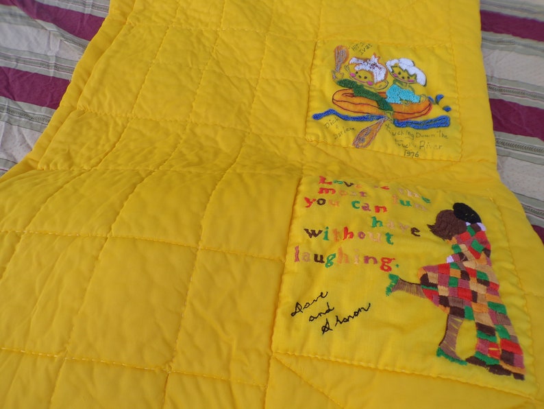 May include: Bright yellow quilt with embroidered images and text. One image depicts two figures in a boat, the other shows two figures embracing. Text includes "Love me...without laughing."