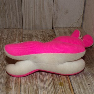 May include: A pink and white plush toy shaped like a rabbit. The toy is lying on its side with its head turned to the right. The toy has a white belly and pink ears.