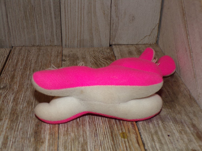 May include: A pink and white plush toy shaped like a rabbit. The toy is lying on its side with its head turned to the right. The toy has a white belly and pink ears.