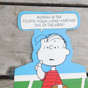 Peut inclure: Une illustration de dessin anim&eacute; de Charlie Brown tenant un ballon de football et disant "MONDAY IS THE FOURTH-DOWN-LONG-YARDAGE DAY OF THE WEEK!"