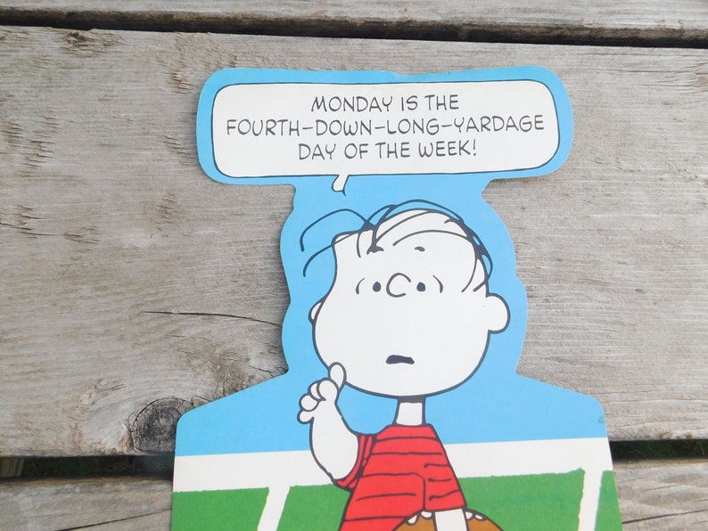 Peut inclure: Une illustration de dessin anim&eacute; de Charlie Brown tenant un ballon de football et disant "MONDAY IS THE FOURTH-DOWN-LONG-YARDAGE DAY OF THE WEEK!"