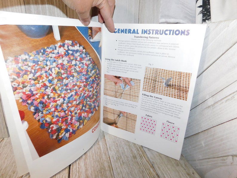 May include: A close-up of a book with instructions on how to use a latch hook to create a rug. The book shows a finished rug made of colorful fabric scraps, as well as diagrams of how to fill the canvas with fabric or fleece.
