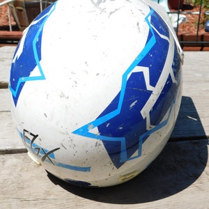 May include: White motorcycle helmet with blue and light blue star-shaped designs. The helmet has a worn look with some scratches and scuffs.
