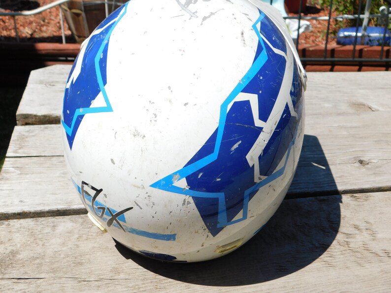May include: White motorcycle helmet with blue and light blue star-shaped designs. The helmet has a worn look with some scratches and scuffs.