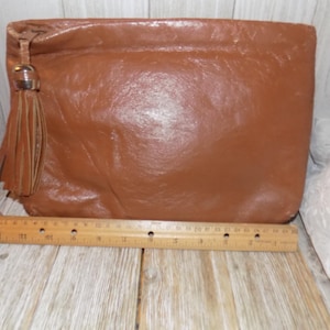 May include: A brown leather clutch with a tassel and a metal accent. The clutch is about 10 inches long.