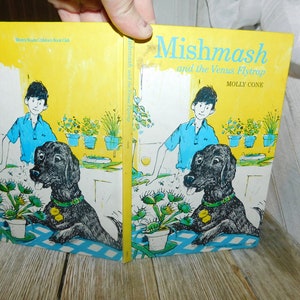 May include: A yellow book cover with the title "Mishmash and the Venus Flytrap" by Molly Cone. The cover features a boy and a black dog in a kitchen setting with plants.