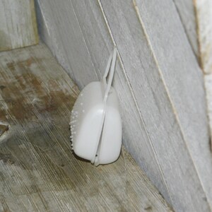 Op de afbeelding: Een witte, plastic, scharnierende container met een getextureerd oppervlak en een lusgreep. De container is open en onthult de binnenkant. Het item is geplaatst tegen een houten oppervlak.