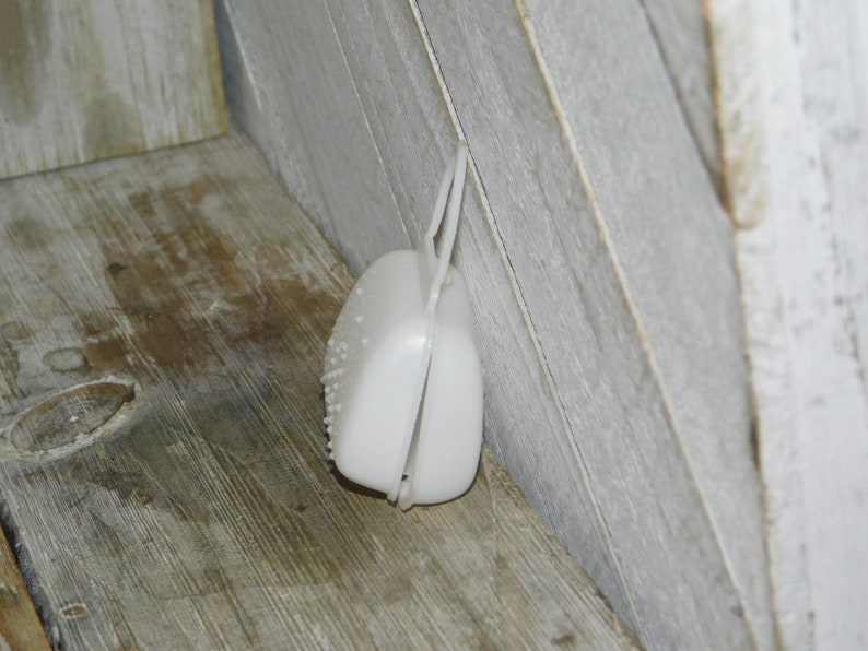 Op de afbeelding: Een witte, plastic, scharnierende container met een getextureerd oppervlak en een lusgreep. De container is open en onthult de binnenkant. Het item is geplaatst tegen een houten oppervlak.
