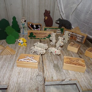 May include: A set of wooden toy figures and blocks, including a girl, a bear, a wolf, a cow, a dog, and several sheep. The figures are painted in bright colors and have simple, childlike designs. The blocks are made of natural wood and have various shapes and sizes.