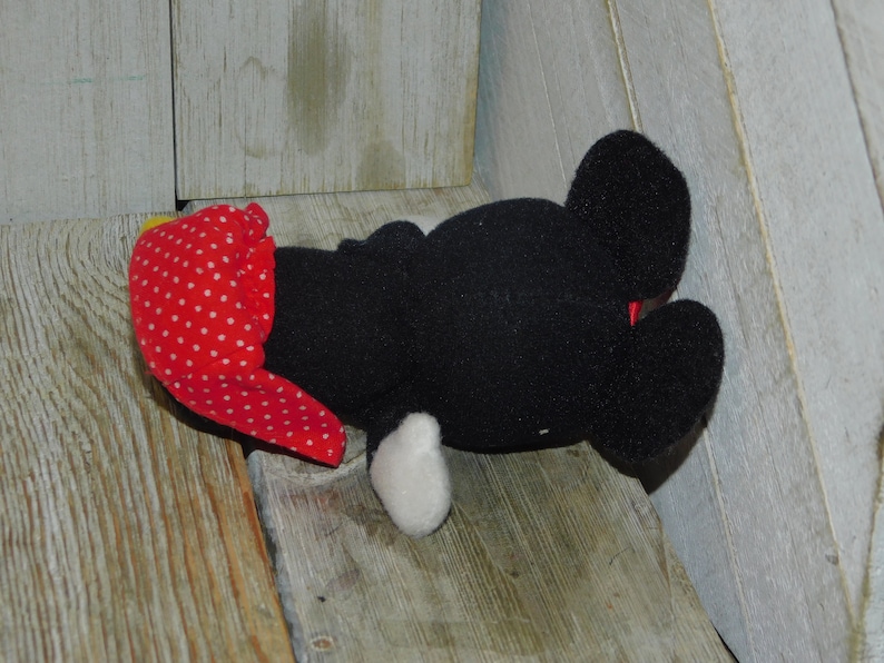 May include: Black and white plush toy with red polka dot fabric on its head. The toy is lying on its back with its legs in the air.
