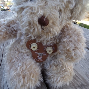 Puede incluir: Un oso de peluche beige con una nariz marrón y una radio unida a su pecho. La radio tiene una cubierta de cuero marrón con botones para el volumen, la sintonización y un interruptor de encendido/apagado. La radio está etiquetada como "Radio Shack" y "Hecho en China".