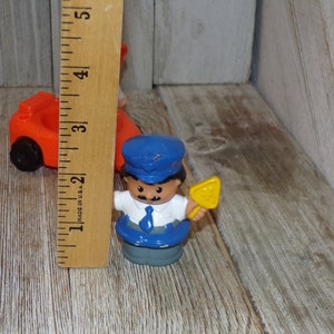 May include: A blue and yellow plastic toy figure of a person wearing a blue hat and a blue and white shirt. The figure is holding a yellow shovel.