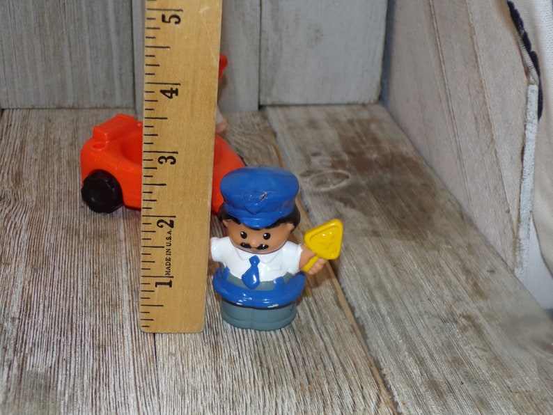 May include: A blue and yellow plastic toy figure of a person wearing a blue hat and a blue and white shirt. The figure is holding a yellow shovel.