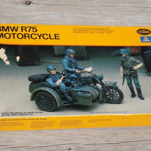 May include: A model kit box for a BMW R75 motorcycle. The box is yellow and orange with the text "BMW R75 MOTORCYCLE". The kit includes a motorcycle with a sidecar and three figures. The actual body length is 21 inches.