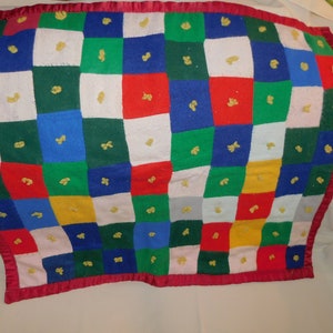 May include: A colorful patchwork quilt with a red border. The quilt is made of squares of different colors, including red, blue, green, yellow, and white. Each square has a small yellow flower embroidered in the center.