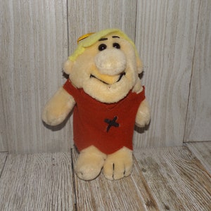 May include: A plush toy of a cartoon character with blonde hair, a red shirt, and a big smile. The toy is about 10 inches tall and is made of soft, cuddly material.