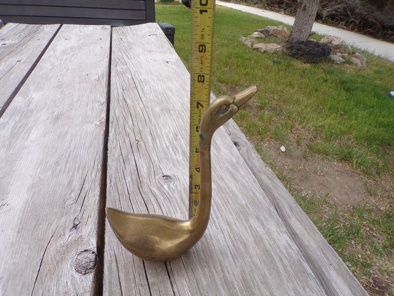 Pu&ograve; includere: Una statuetta di cigno in ottone con un collo lungo e una testa dettagliata. Il cigno &egrave; alto circa 18 cm ed &egrave; seduto su una superficie di legno.