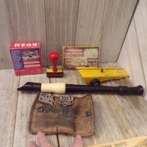 May include: A collection of vintage toys and games including a red wooden stamp, a yellow toy car, a wooden flute, a small brown leather pouch, a box of cards with the word "Bush" on it, and a small wooden plaque with an American flag design.