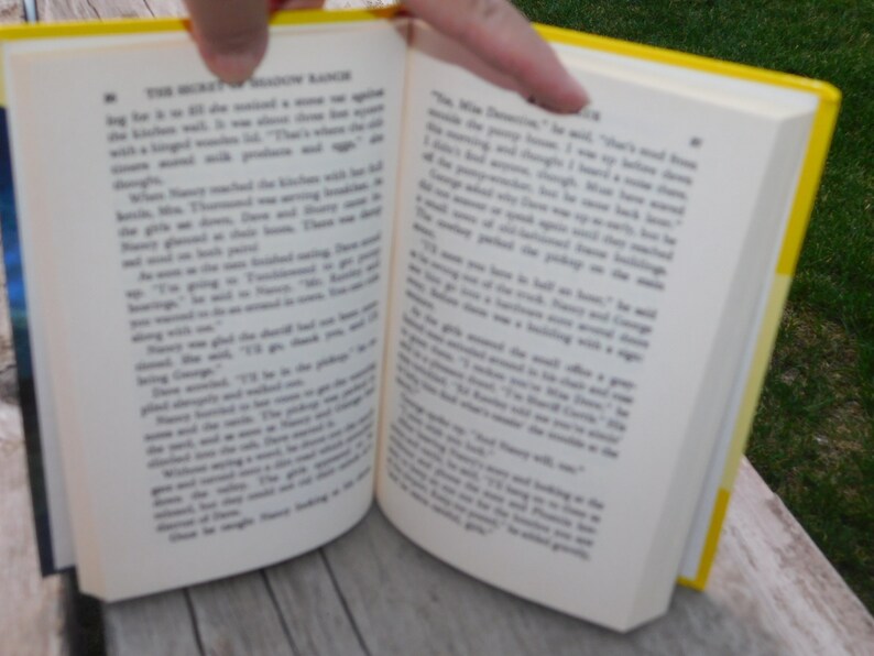 May include: An open book with yellow covers. The pages are filled with text. The book is titled "The Mystery of Shadow Ranch".