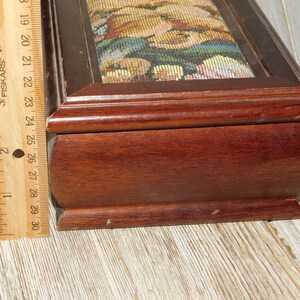 May include: A wooden jewelry box with a hinged lid. The lid is covered in a tapestry fabric with a floral pattern. The box is approximately 9 inches long.