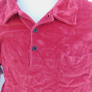 May include: A long-sleeved, red velour shirt with a button-up collar and a single pocket on the left side.