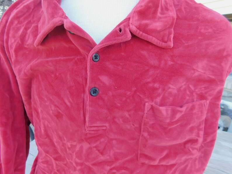 May include: A long-sleeved, red velour shirt with a button-up collar and a single pocket on the left side.